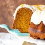 A slice of frosted pumpkin bundt cake on blue cake server, brown background, cake on stand