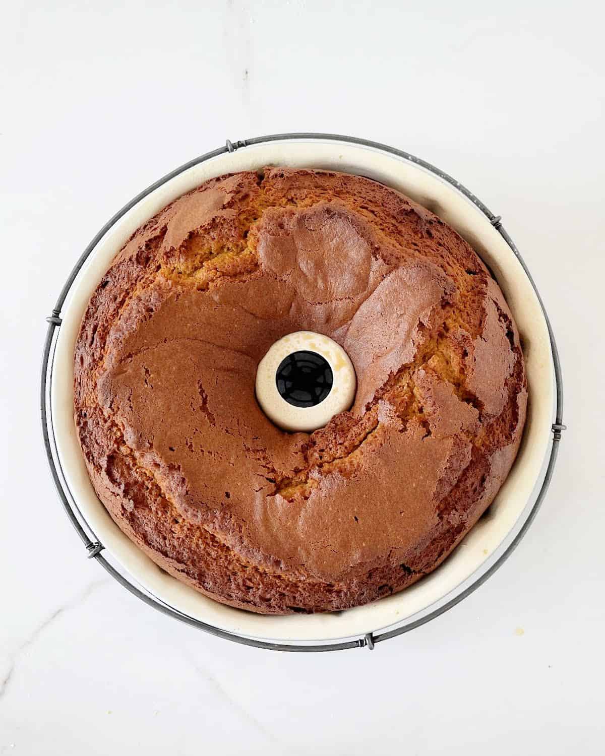 Baked pumpkin bundt cake in the pan on a wire rack. White marbled surface.