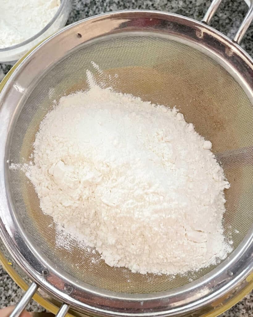 Sifting flour mixture over a bowl.