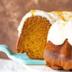 Blue cake server lifting a slice of glazed pumpkin bundt cake. Brown background.