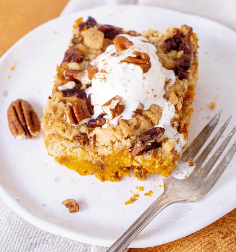 Single serving of pumpkin pecan dump cake on white plate, a fork, white surface