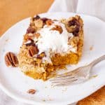White plate with bitten serving of pumpkin dump cake with ice cream on top. White and orange background.