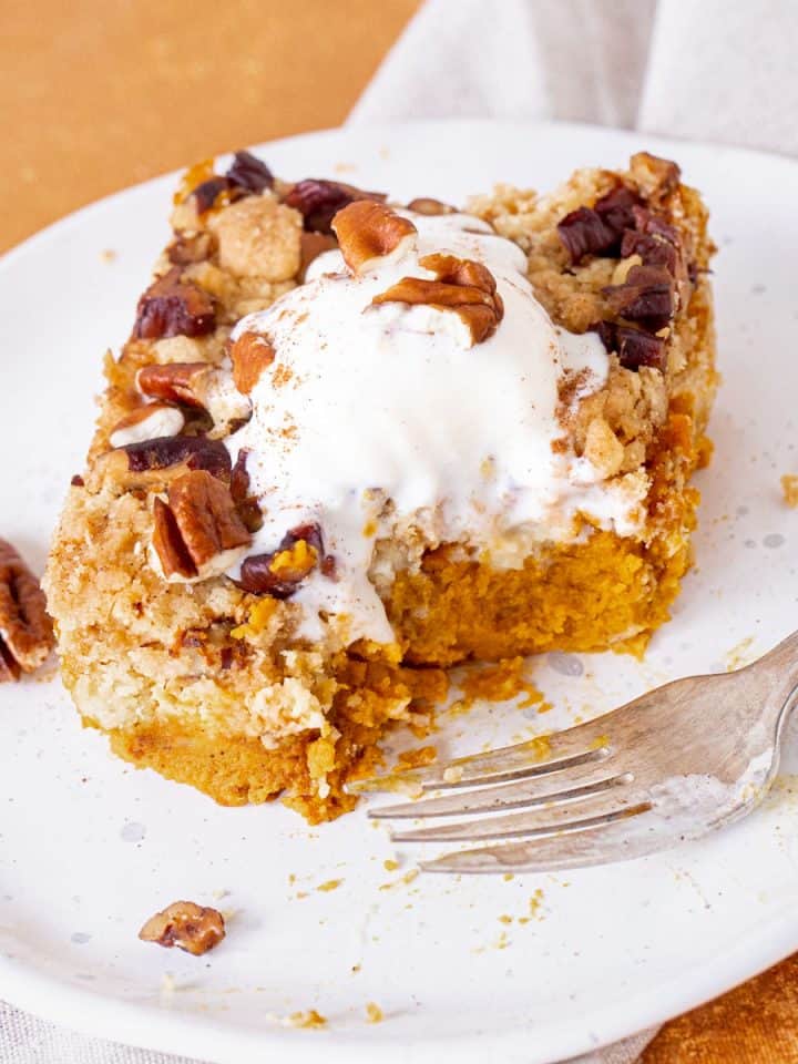 White plate with bitten serving of pumpkin dump cake with ice cream on top. White and orange background.