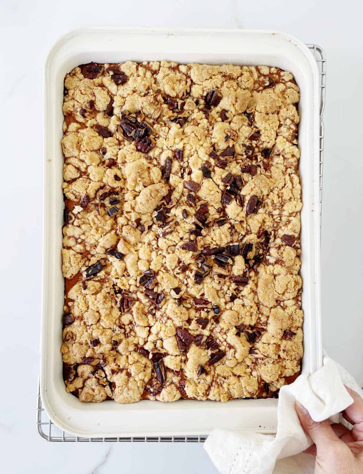 Baked pumpkin dump cake in rectangular pan, white marble surface, a hand with towel holding it.