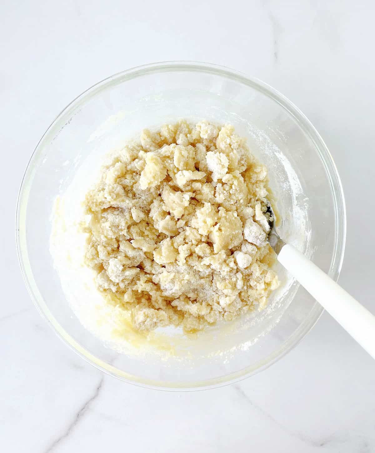 Crumbly dump cake topping on a glass bowl with a white spoon. White marble surface.