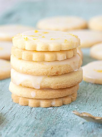 Stack of glazed lemon shortbread cookies on a green colored wooden board.