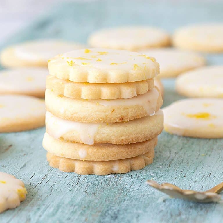 Stack of glazed lemon shortbread cookies on a green colored wooden board.