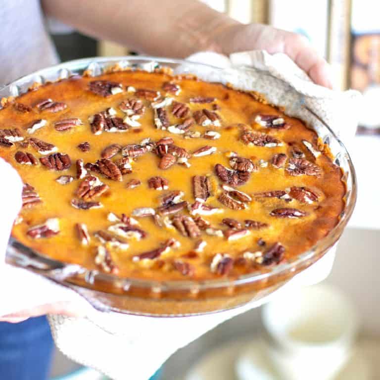 Person holding whole pecan sweet potato pie in glass pie dish