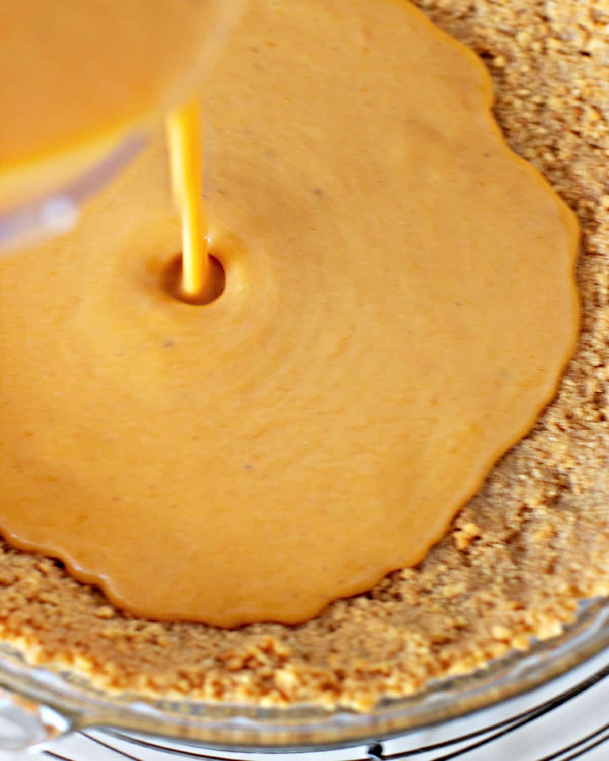 Sweet potato pie filling being poured into a crumb crust.