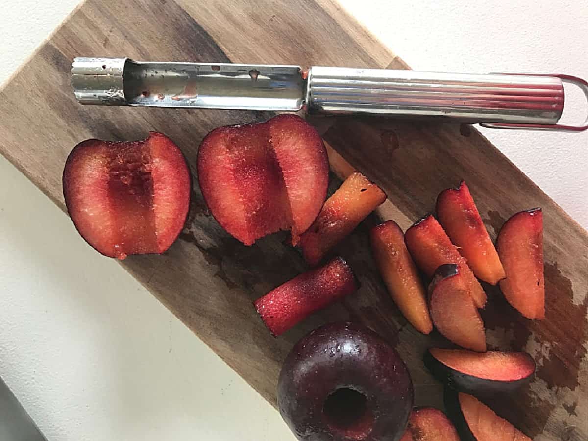 Wooden board on white surface with apple corer and fresh plum slices.