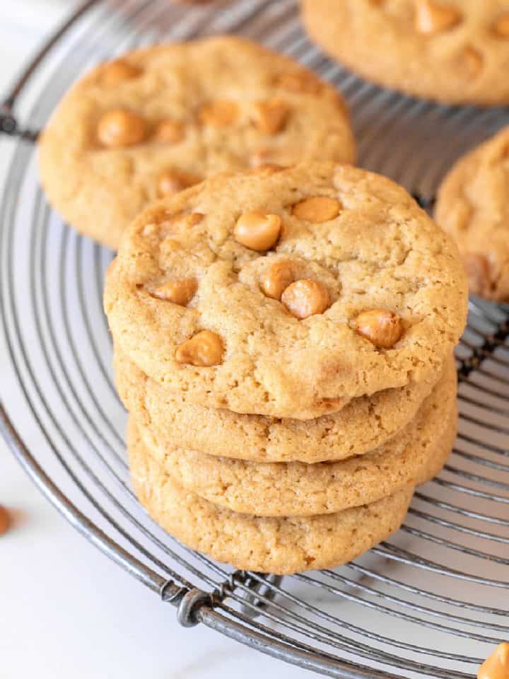 Stack and individual butterscotch cookie son wire rack, white marble surface.