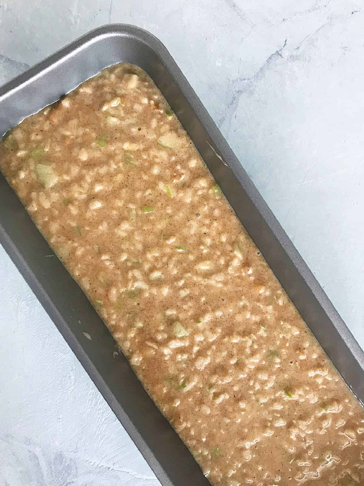 Apple cake batter in a metal loaf pan on a white marble surface.