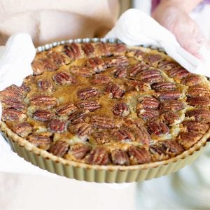 Baked pecan tart held with white kitchen towels.