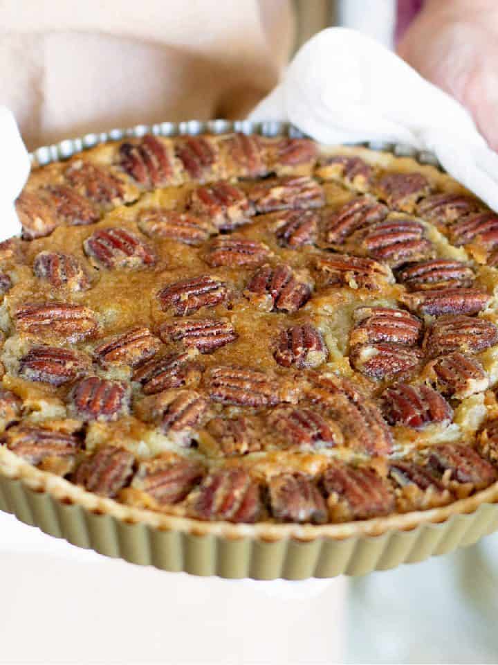 Baked pecan tart held with white kitchen towels.