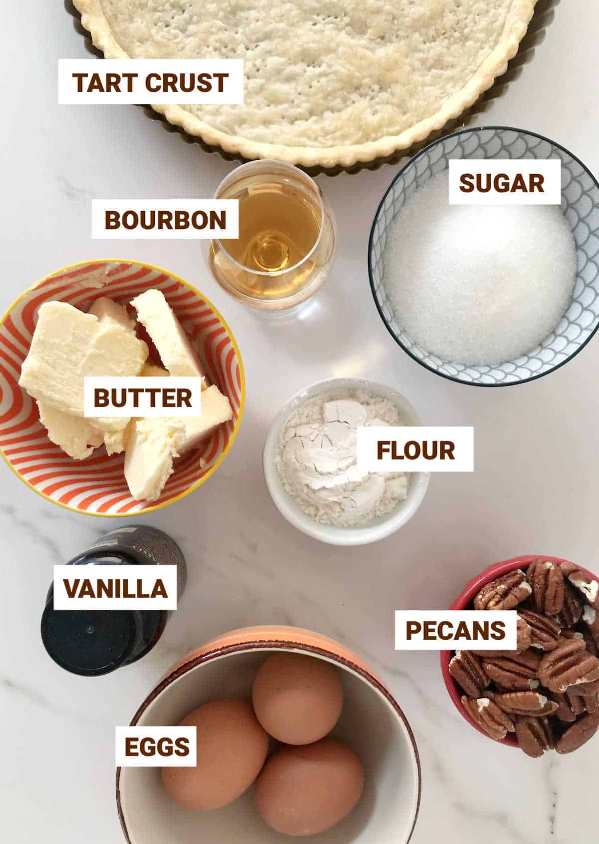 Bourbon pecan tart ingredients in bowls on a white surface, with text overlay. Including eggs, butter, sugar, flour, vanilla.