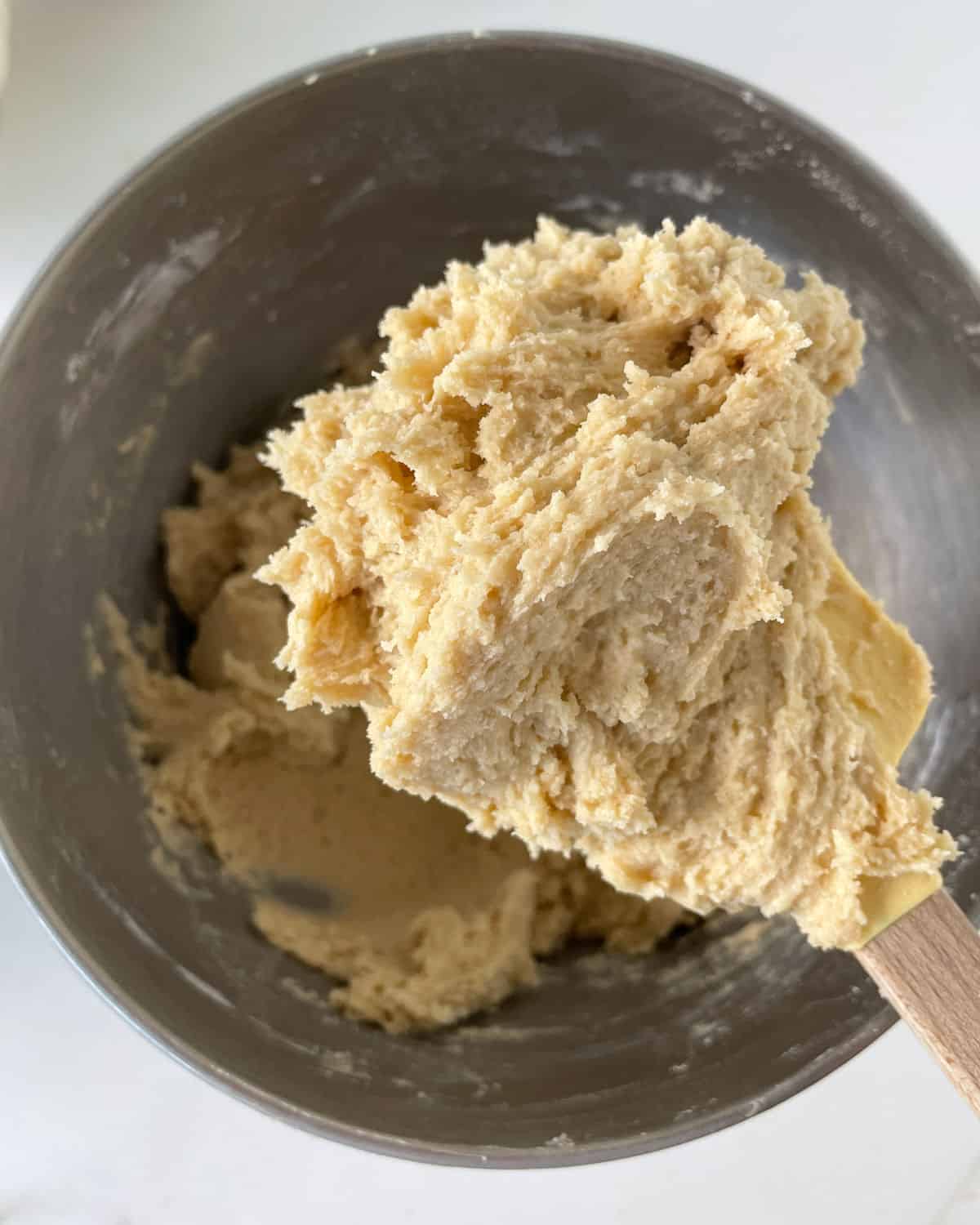 Cookie dough on a wooden spoon above the metal bowl with rest of batter.