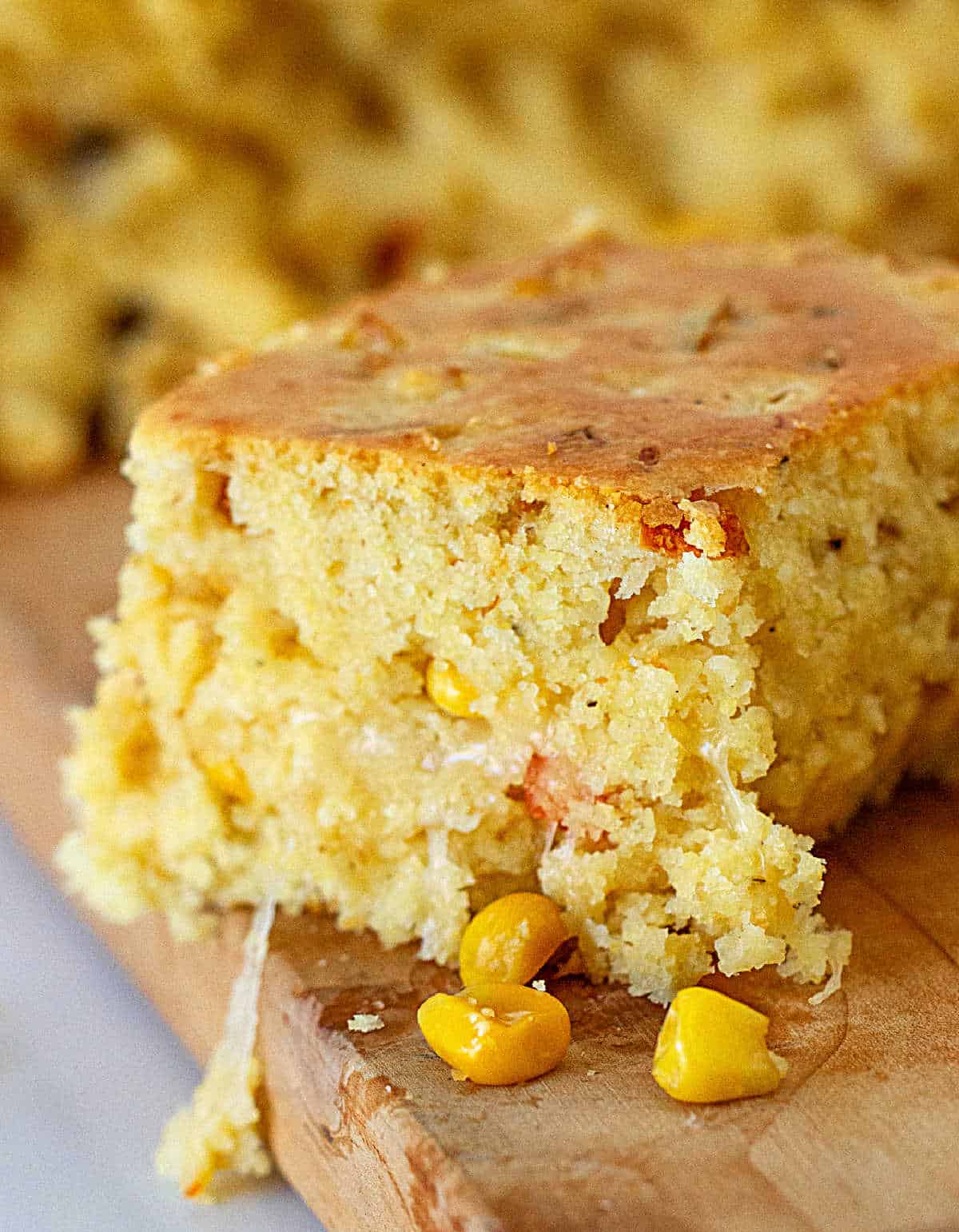 Close up image of cheese cornbread square on wooden board