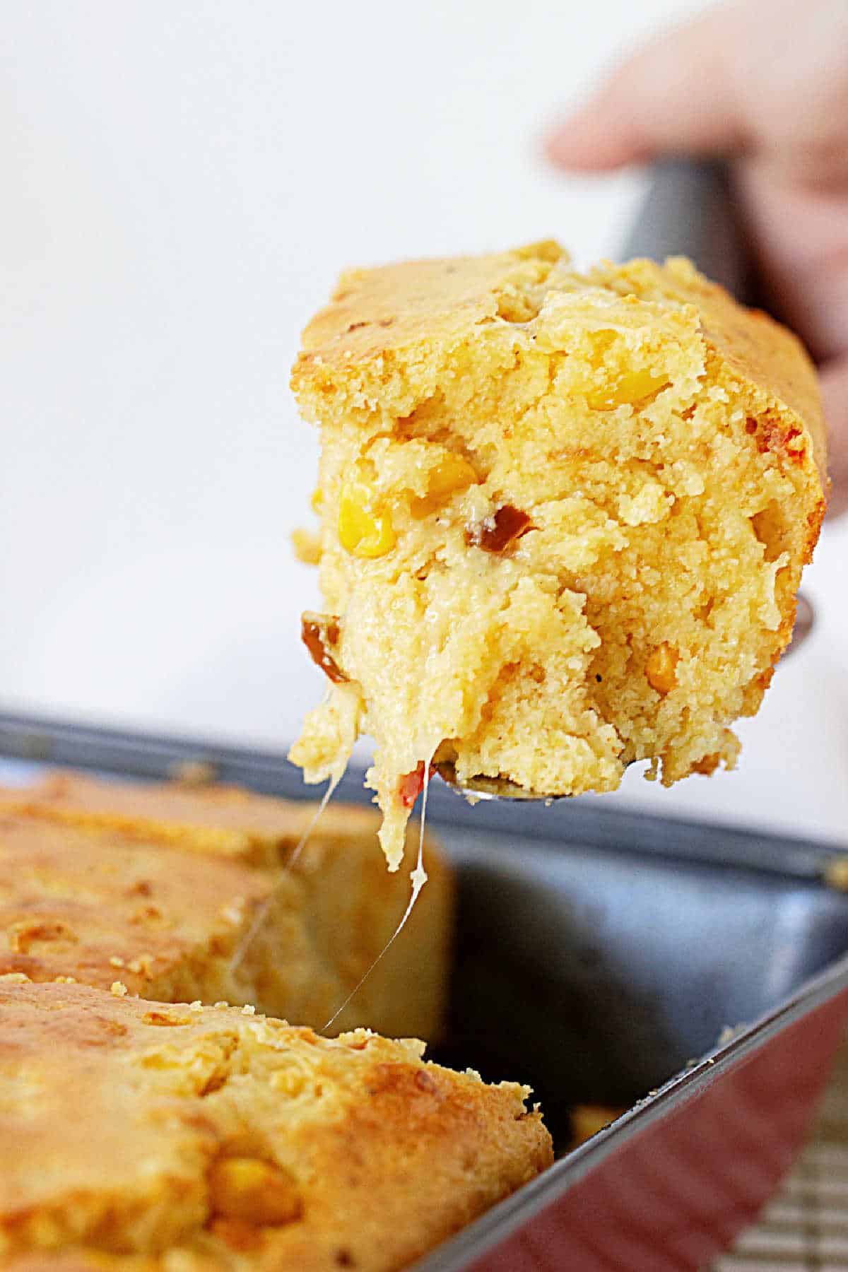 Cheesy piece of cornbread on a cake server over the metal pan with rest of bread.