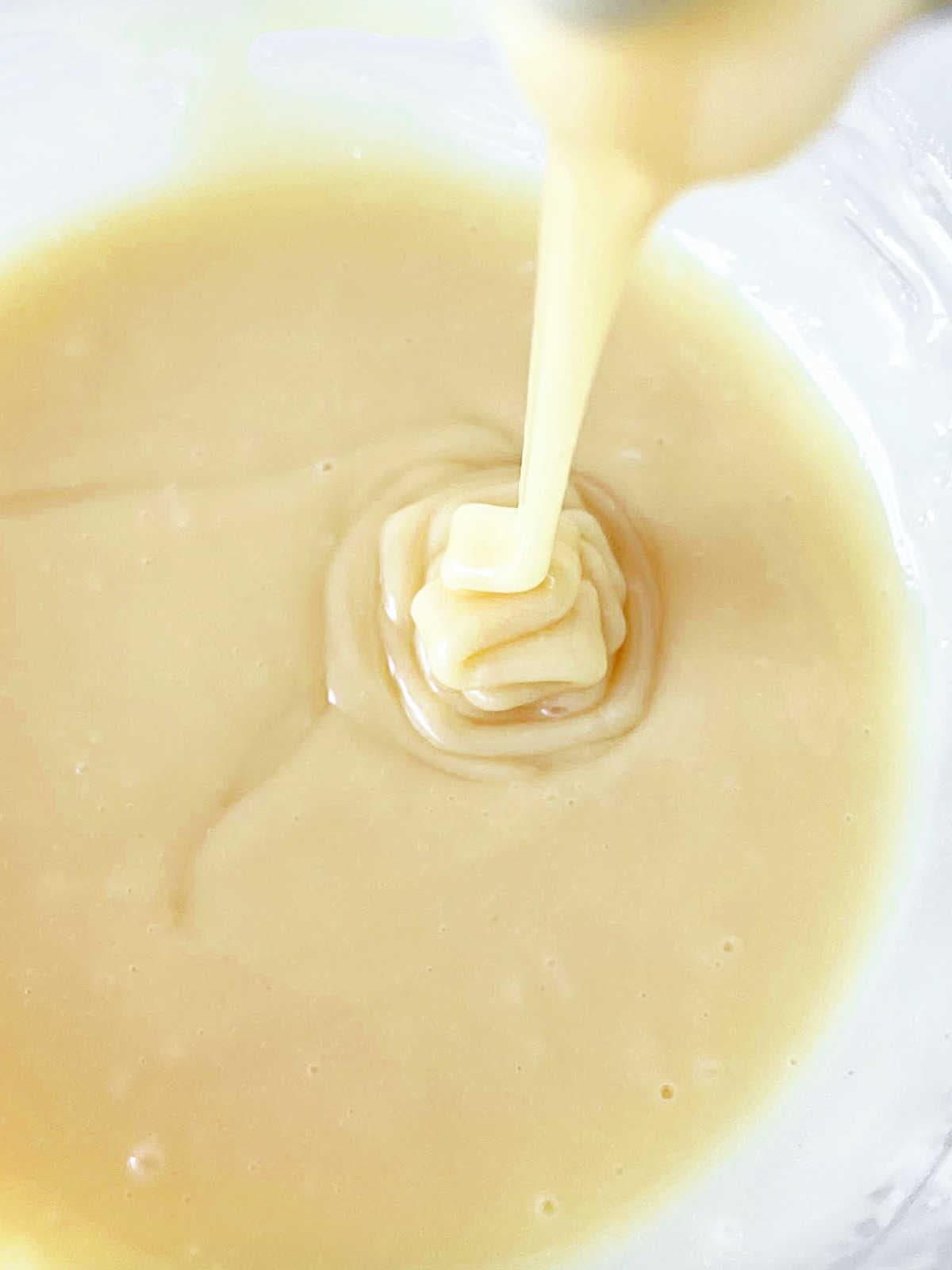 Melted white chocolate drizzling into a glass bowl.