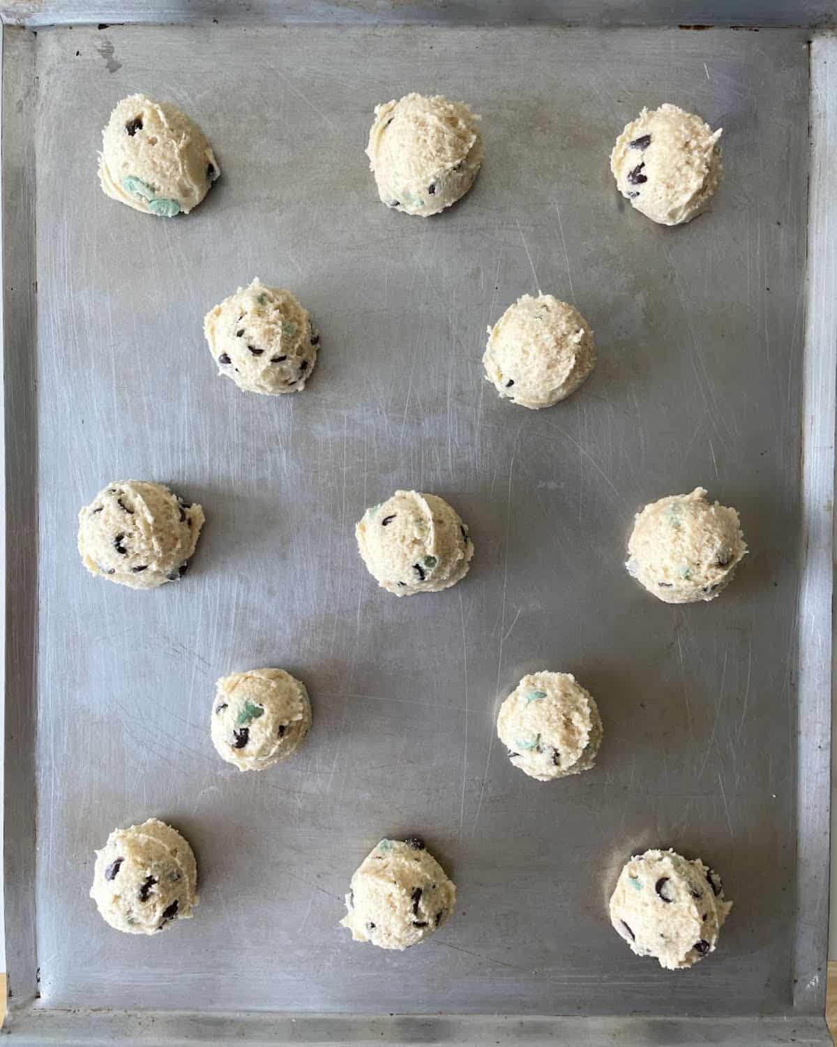 Metal cookie sheet with scoops of mint chip cookie dough. 