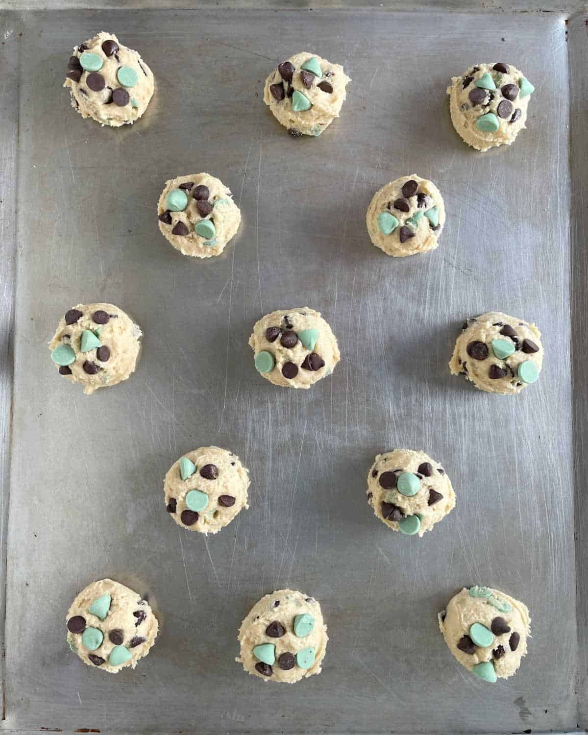 Several scoops of mint and chocolate chip cookie dough on a metal baking sheet.
