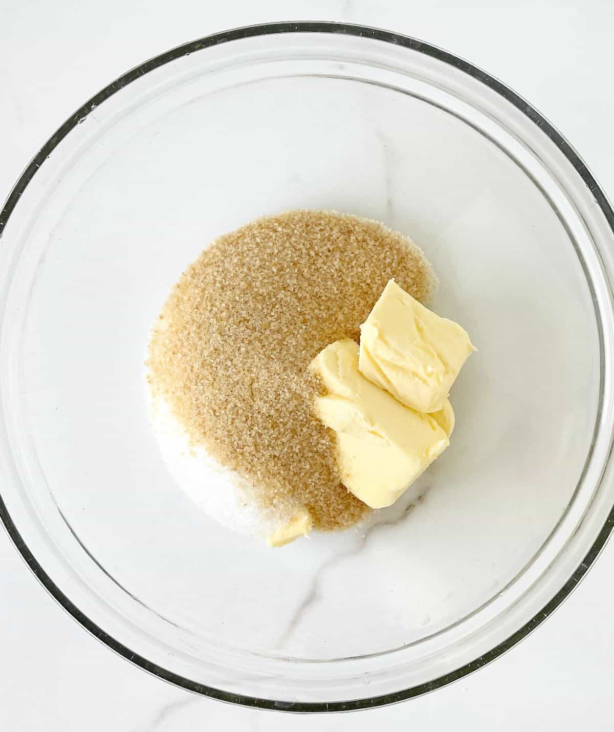 Top view of brown sugar and butter in a glass bowl on a white surface.