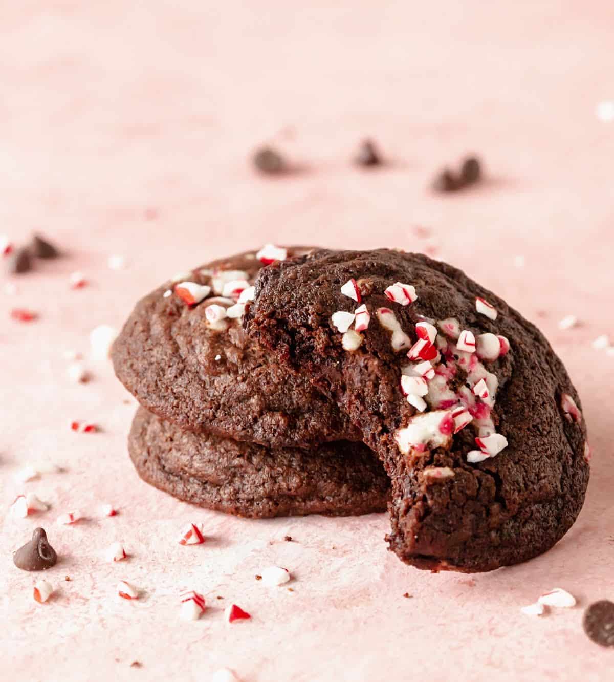 Stack of three chocolate peppermint cookies, one bitten, pink background