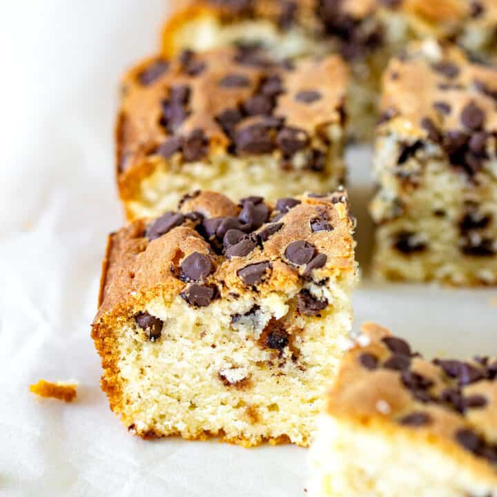 Squares of vanilla cake with chocolate chips on parchment paper.