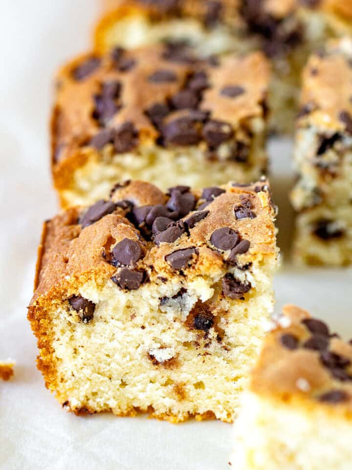 Squares of vanilla cake with chocolate chips on parchment paper.