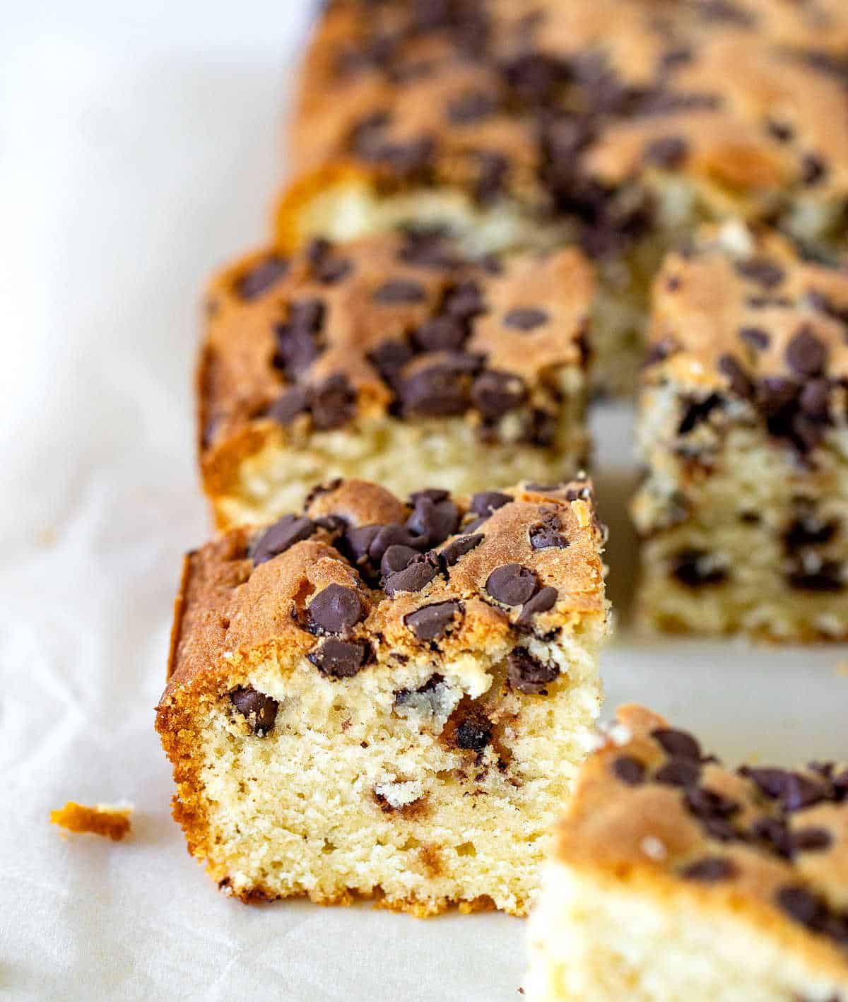 Squares of vanilla cake with chocolate chips on parchment paper.
