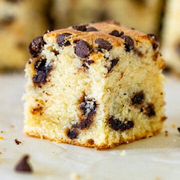 Single square of vanilla cake with chocolate chips on a white surface.