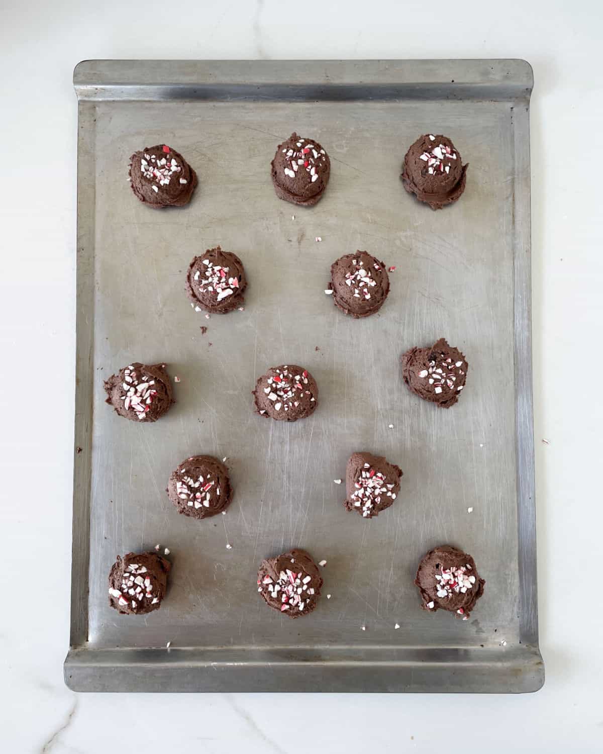 Metal baking sheet with chocolate cookie dough balls with crushed peppermint candy. Top view.