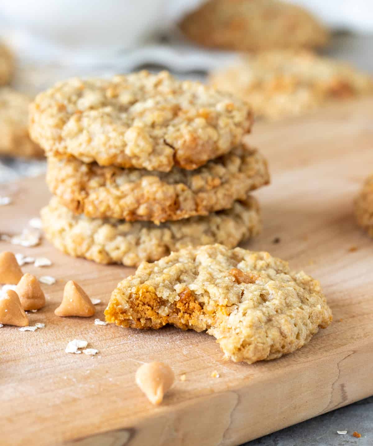Bitten butterscotch oatmeal cookie on wooden board, stack of cookies in background
