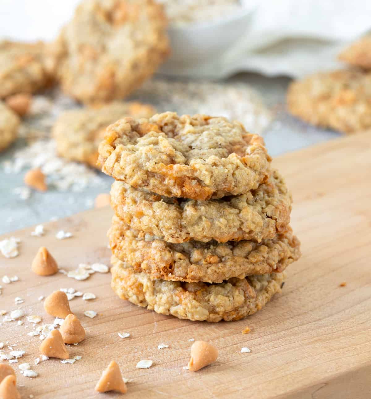 Stack of oatmeal butterscotch cookies on wooden board, loose chips around