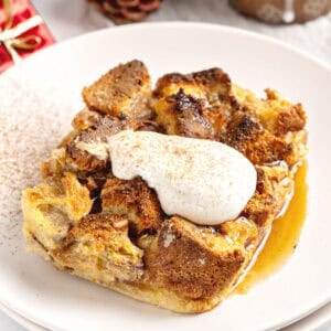 Serving of panettone bread pudding with cream and cinnamon. White plate.