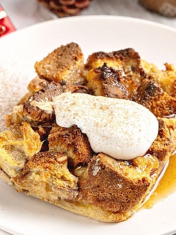 Serving of panettone bread pudding with cream and cinnamon. White plate.