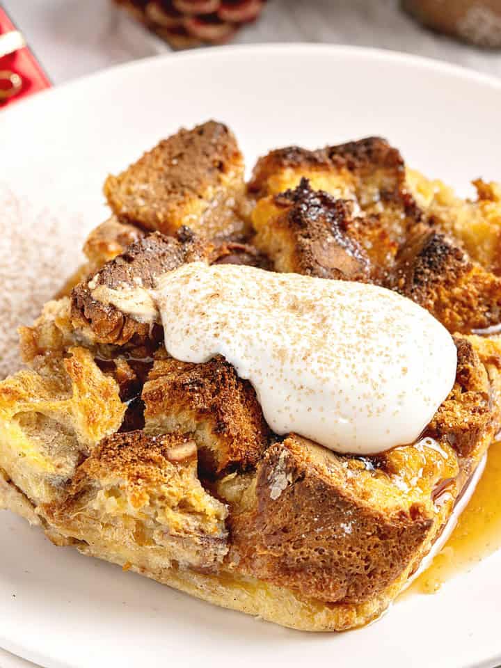 Serving of panettone bread pudding with cream and cinnamon. White plate.