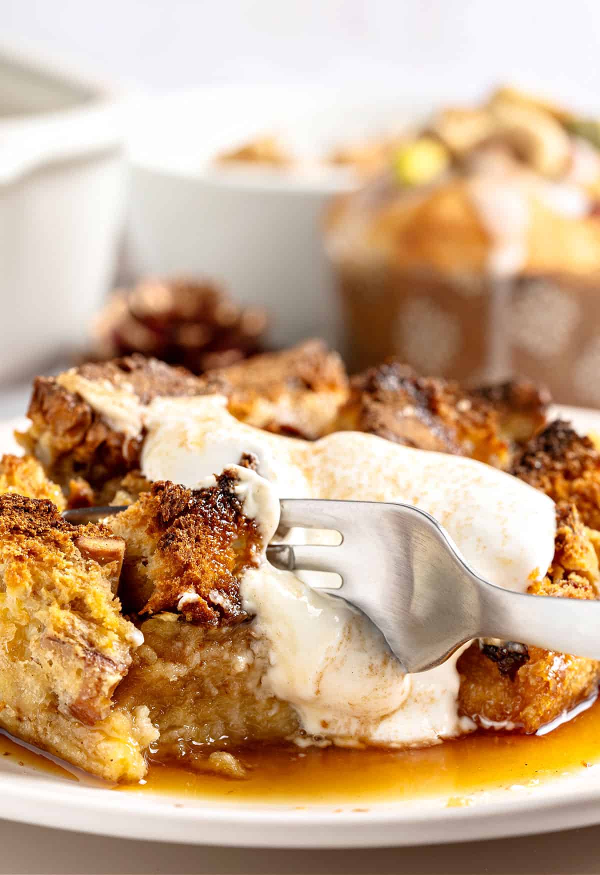 Forking a serving of cream-topped panettone bread pudding, White plate and background.