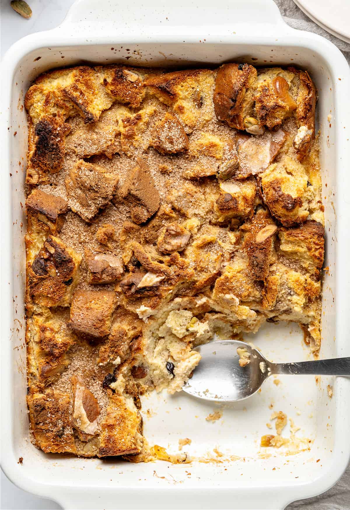 Serving missing in white baking dish of panettone bread pudding. Silver spoon inside. Top view.