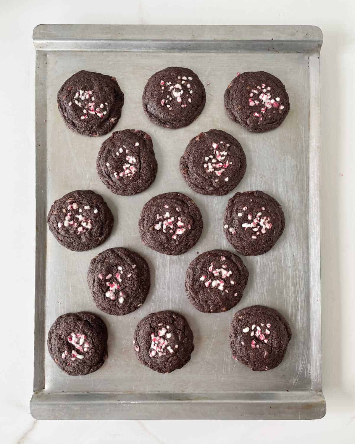 Top view of baked chocolate cookies with crushed peppermint candy on a metal baking sheet.