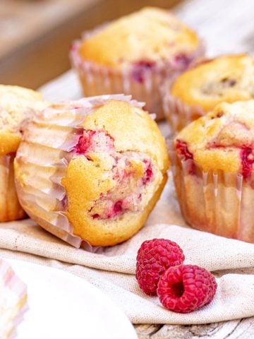 Close up of four raspberry muffins on linen napkin and grey wooden surface