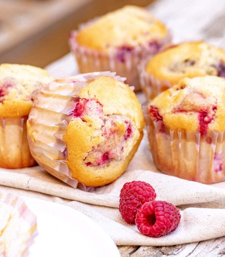Close up of four raspberry muffins on linen napkin and grey wooden surface