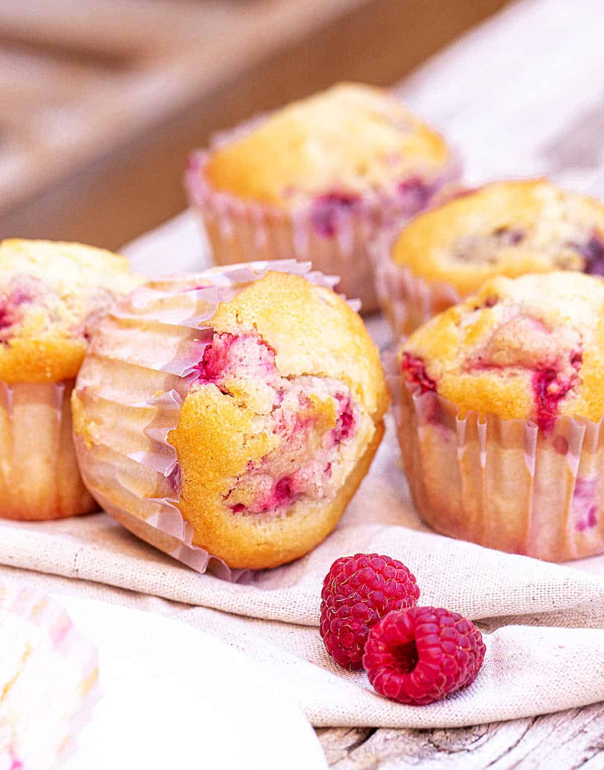 Golden raspberry muffins in paper cups on a grey beige surface.