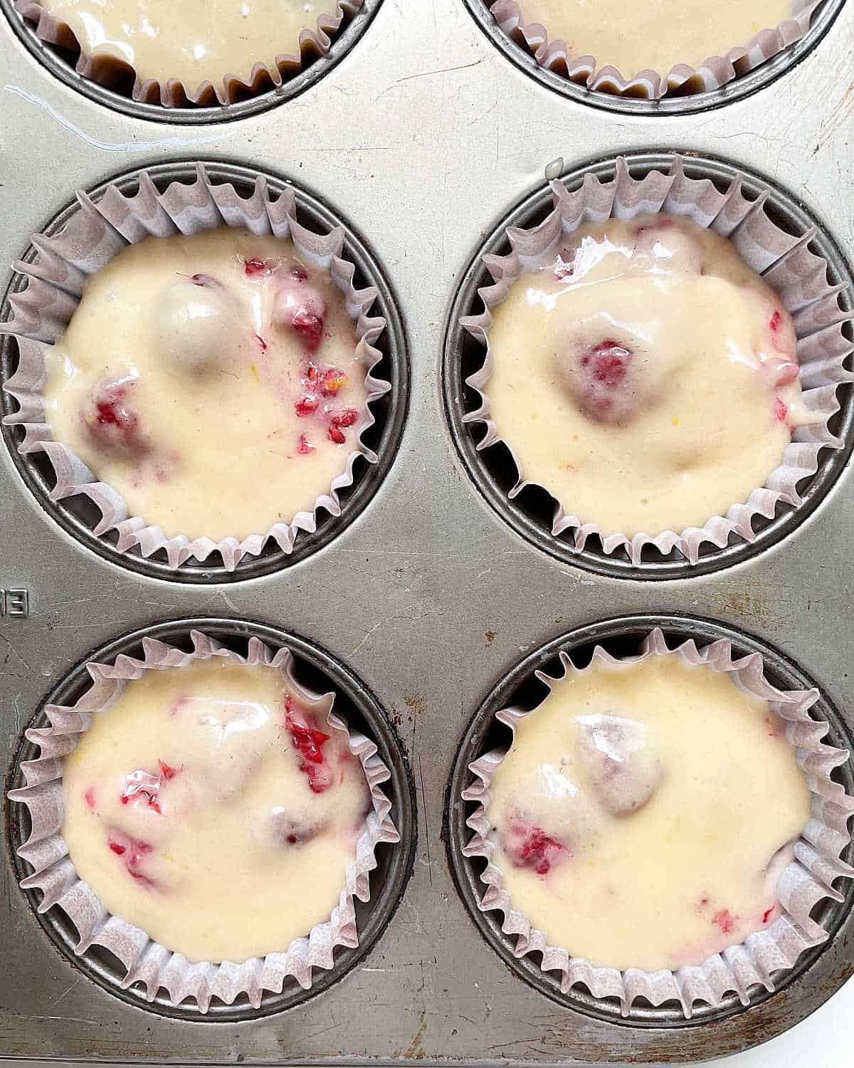 Close up of unbaked raspberry muffins in paper liner in a metal pan. 