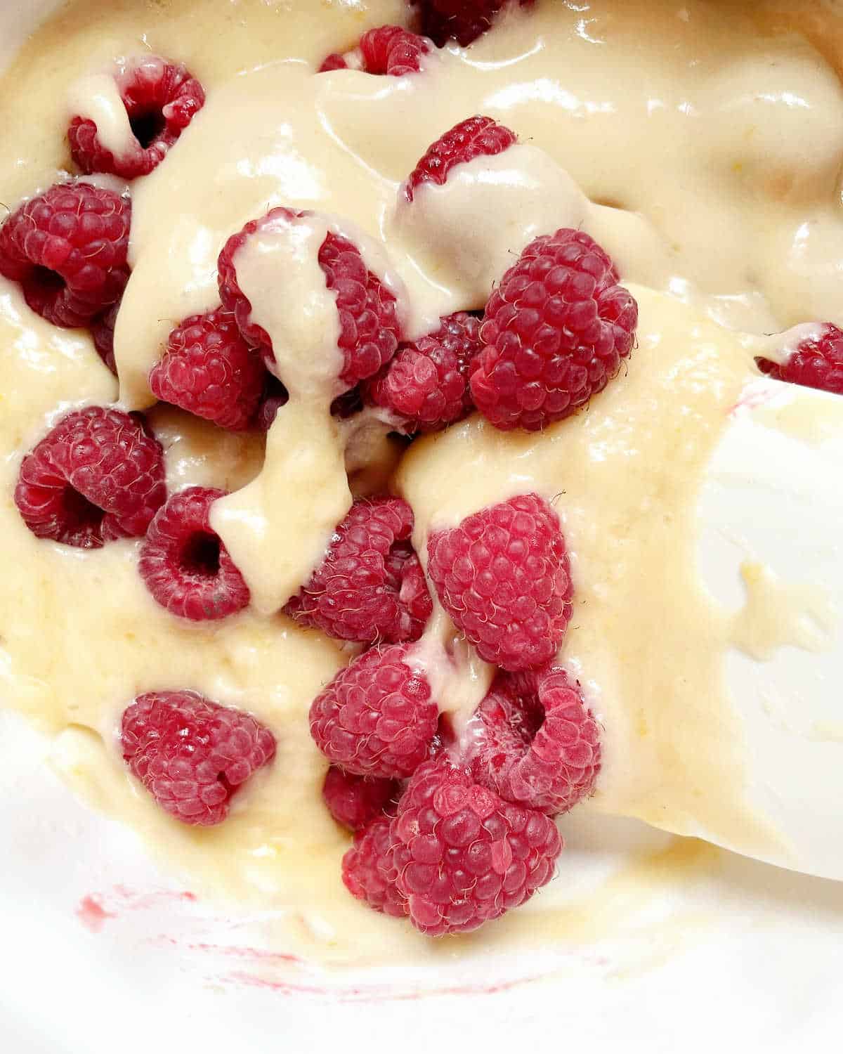 Folding in fresh raspberries into muffin batter with a white spatula.