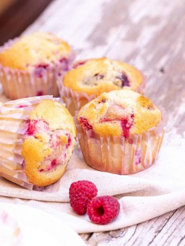 Grey wooden surface with raspberry muffins in paper cups