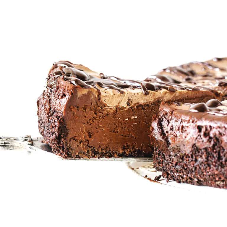Cake server lifting slice of chocolate cheesecake from whole cake, white background.