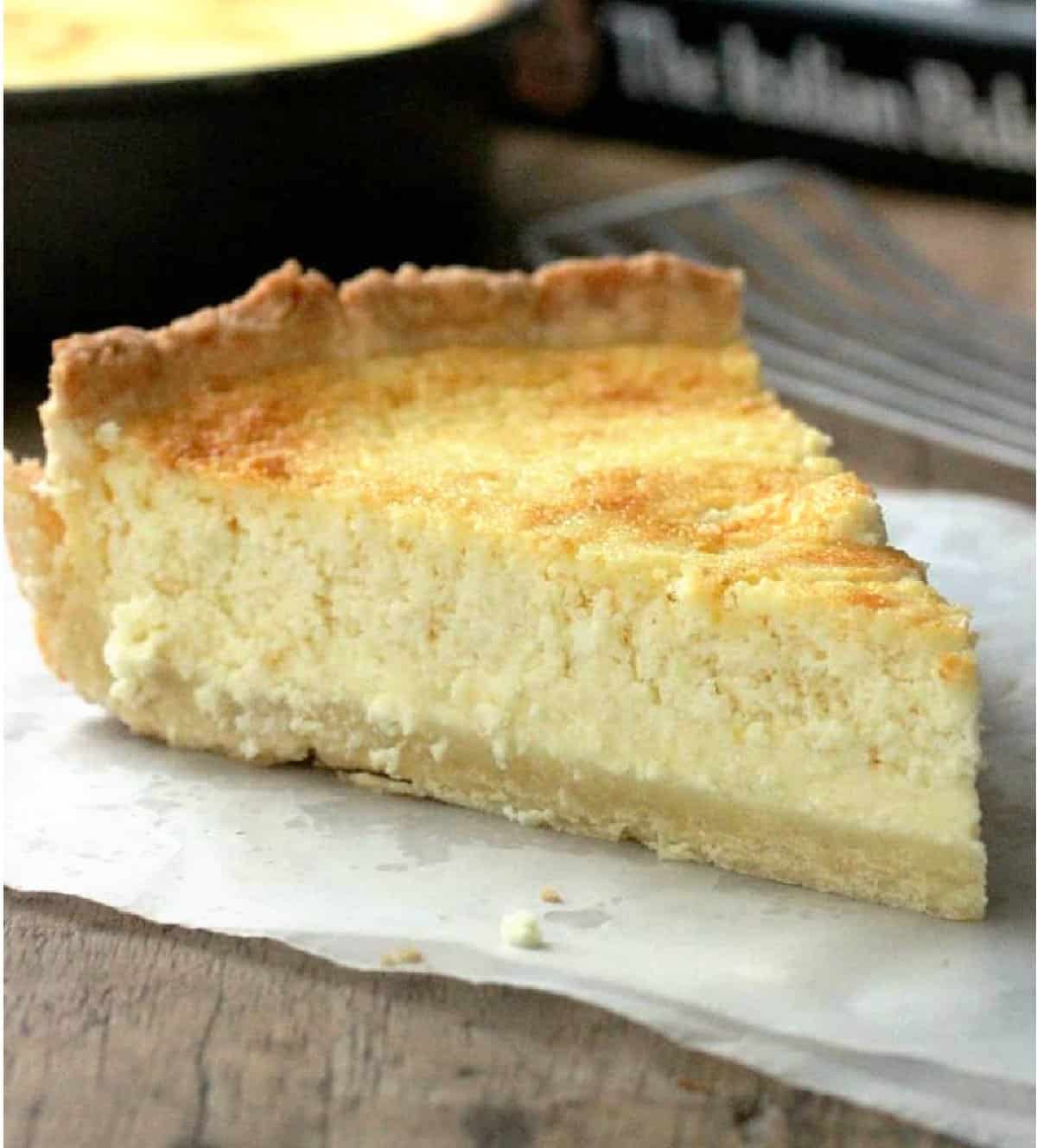 One slice of ricotta pie on parchment paper, pan and book in background