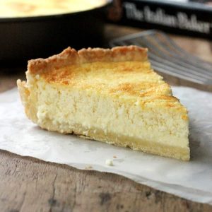 Close up of ricotta pie slice on parchment paper over wooden table