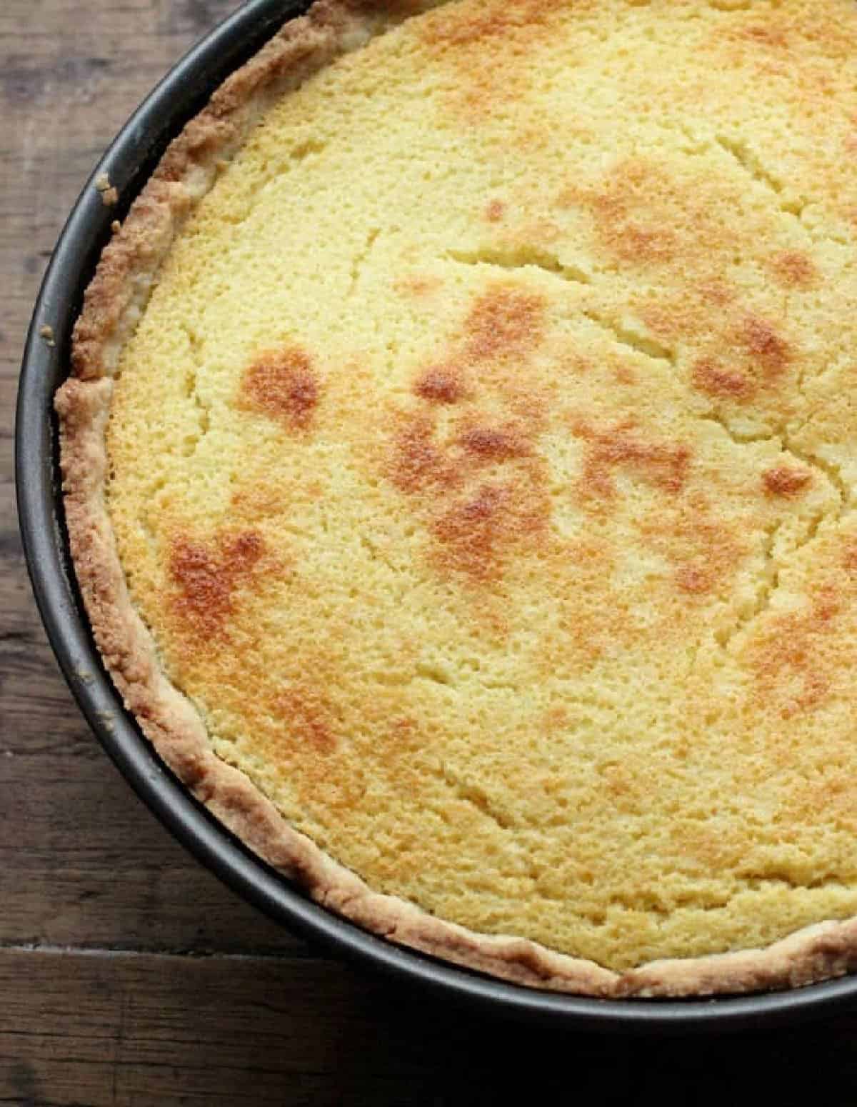 Top view of partial ricotta pie in pan on wooden table